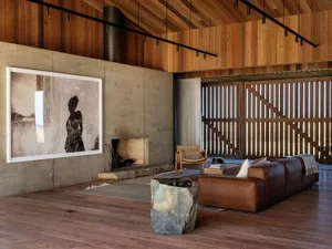 A modern industrial living room with concrete walls, wooden flooring, and a large framed black and white photograph of a beac