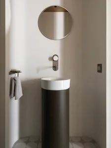 A minimalist bathroom with a ceramic vessel sink on a cylindrical black pedestal, above a round mirror, and featuring geometr