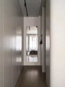A minimalist bedroom featuring white walls, a white bed, and a wooden floor.