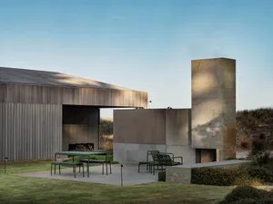 A modern residential exterior with a concrete fireplace and green seating area.