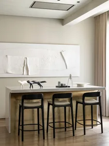 A modern kitchen with a concrete countertop featuring sleek bar stools and decorative sculptures.