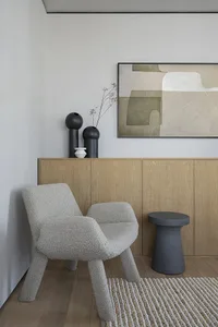 Modern living room featuring a textured cushion on a wooden chair, a wooden cabinet with black vases, and a large abstract ar