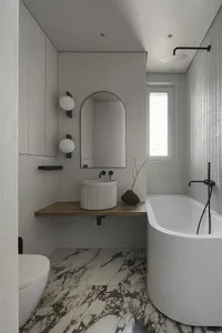 Modern minimalist bathroom with a white bathtub, wooden vanity, and marble floor tiles.