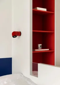 A modern, minimalist bedroom featuring a red bookshelf with a wall-mounted lamp.