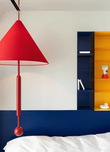 A minimalist bedroom with concrete walls, a red pendant light, and a white bed.