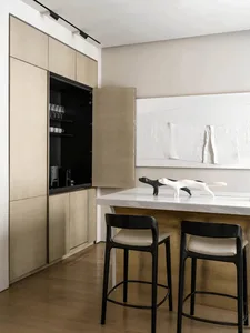 A modern minimalist kitchen with a wooden cabinet and island, white countertop, and black stools.