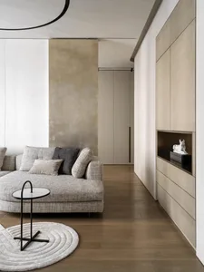 A modern minimalist living room featuring a wooden floor, a grey sectional sofa adorned with cushions, and a small round tabl