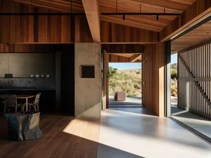 Modern residential interior featuring exposed wood beams, concrete flooring, and a natural outdoor view through large windows