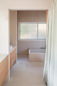 Minimalist bathroom with concrete floor, walls, and bathtub, glass window, and light-colored curtain.