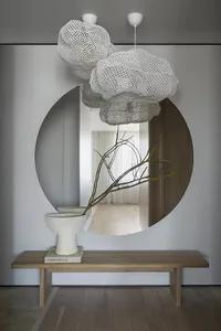 Modern minimalist entryway decorated with airy, white cloud-like lighting fixtures, a round mirror reflecting a serene interi