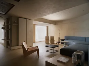 A minimalist interior with concrete elements, featuring a blue sofa, wooden chairs, and a coffee table.