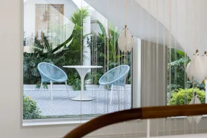 A minimalist outdoor living area featuring metallic wicker chairs and a round table surrounded by lush greenery.