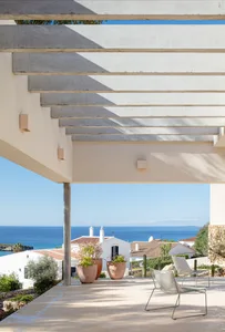 A modern interior space featuring a concrete patio area with porcelain tiles, a pergola structure, and a view of oceanfront h