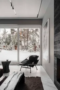 Modern living room with a view of a snowy cityscape, featuring a black lounge chair with a fur blanket, a wooden bench, and a