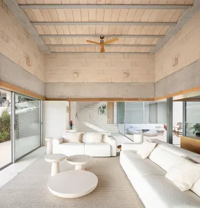 A modern living room with concrete walls and ceiling, featuring white sofas, white coffee tables, and a spiral staircase.
