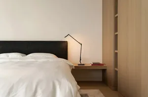 A modern minimalist bedroom featuring a bed with white bedding, a black headboard, and a wooden nightstand with a black lamp