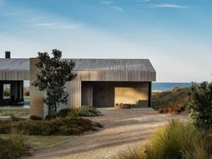 Modern minimalist residential exterior featuring concrete and wooden materials, with a small tree and a path leading to a gar