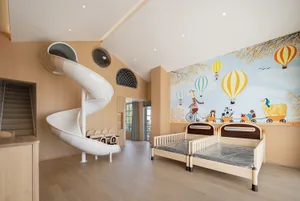 A children's room featuring a wooden slide and beds with a mural of hot air balloons and animals on the wall.