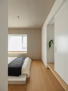 A minimalist bedroom featuring a wooden floor, metallic headboard, and fabric bedding.