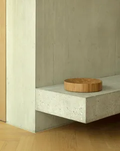 A minimalist interior design featuring a concrete shelf with a circular wooden object on it.