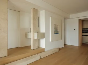 Modern residential entryway with minimalist design, featuring a concrete pillar and wood floor.