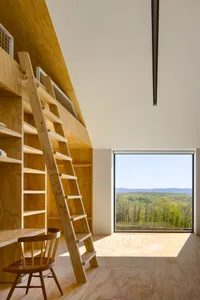 A modern home office with a wooden ladder, wooden table, and a large window overlooking green mountains.