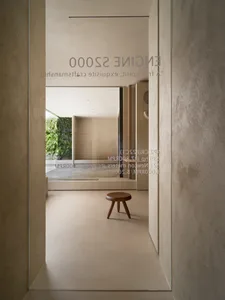 A minimalist living space with concrete walls and floor, featuring a wooden stool and greenery.