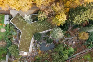 Aerial view of a wooden and stone resort with a green roof surrounded by autumn foliage.