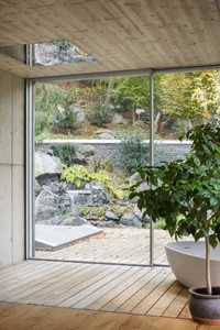Bathroom with minimalist design, wooden floors, and large windows overlooking a garden with a waterfall.