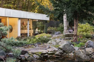 A minimalist garden featuring concrete structures, stone pathways, and glass elements surrounded by natural foliage and autum