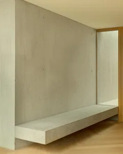 A minimalist interior with a concrete floating shelf against a concrete wall on a light-colored hardwood floor.