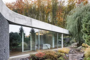 A modern home with large glass windows and concrete exterior surrounded by autumn foliage.