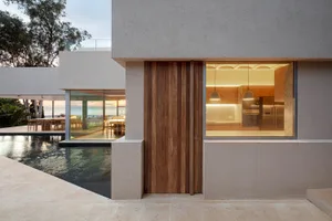 Modern beach house entry with a wooden door and large windows showing the interior.