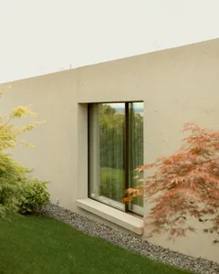 A modern house with a concrete exterior, surrounded by greenery with a window overlooking a serene landscape.