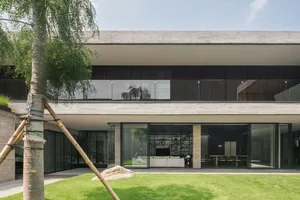 A modern concrete living room with large windows and greenery.