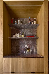 A home bar with wooden shelves and a marble countertop displaying various bottles of liquor and glasses.