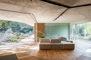 Interior of a modern living room with wooden walls and floor, large windows, and minimalist furniture.