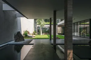 A minimalist residential space featuring concrete walls and floors, with a central courtyard, greenery, and water feature.