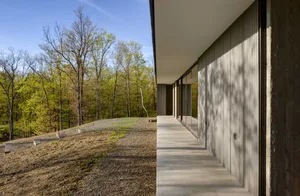 Modern residential building exterior with metal siding and large windows overlooking a forested area.