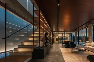 A modern residential interior featuring a wooden staircase, glass railings, and concrete flooring.