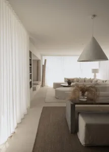 A modern, minimalist living room with neutral furniture and decor, featuring fabric, cement, and concrete elements.