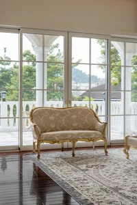 Classical-style sofa with beige upholstery and decorative cushioning, placed on a patterned carpet within a spacious living a