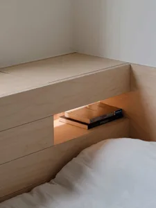A minimalistic bedroom featuring a built-in nightstand made of light-colored wood.