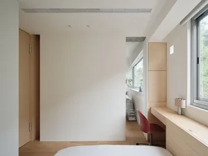 A minimalist bedroom featuring wooden furniture, white walls, and a red desk chair.