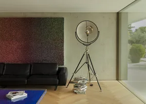 A modern black sofa in a living room with a concrete wall and a colorful wall hanging.