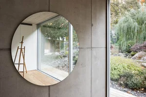 Circular window with concrete walls and a view of a garden with trees and plants.