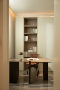 A modern home office with a sleek desk, leather chair, wooden bookshelf, and minimalist interior design.