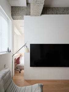 Modern living room with a concrete wall, minimalistic furniture, and a sleek black TV.