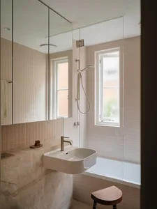 Modern minimalist bathroom with a sink, bathtub, and shower in a beige-tiled bathroom with marble accents and glass window.
