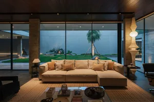 Modern minimalist living room with concrete and glass walls, wooden floor, and a comfortable sofa adorned with cushions.